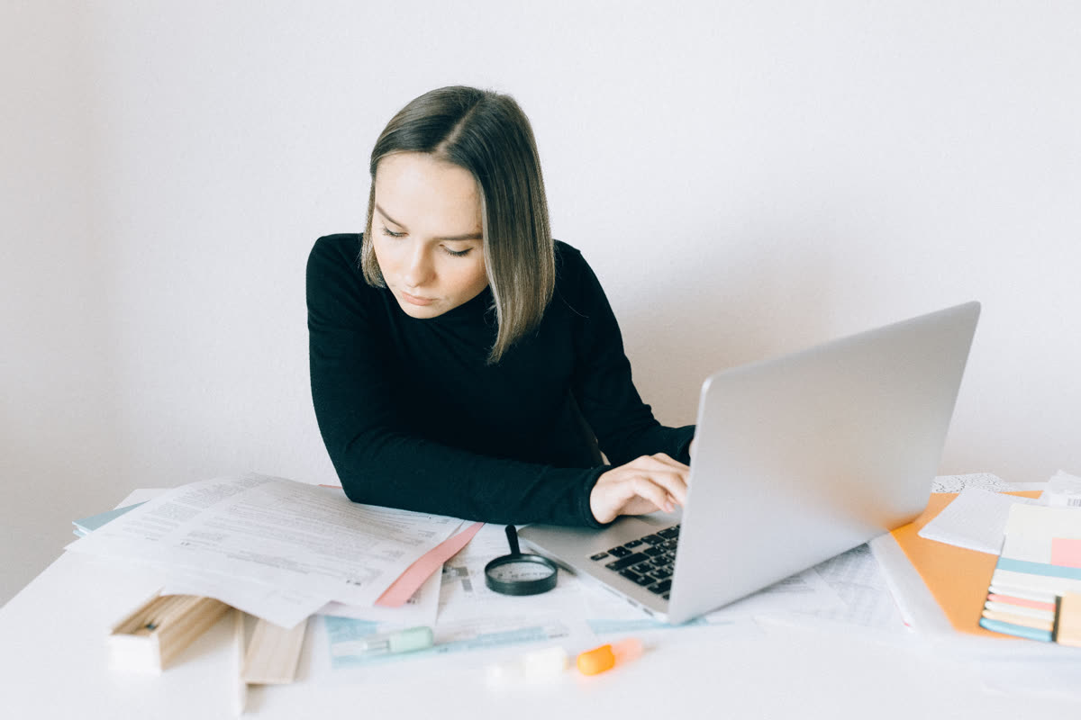 Woman researching at a desk with documents and a laptop.