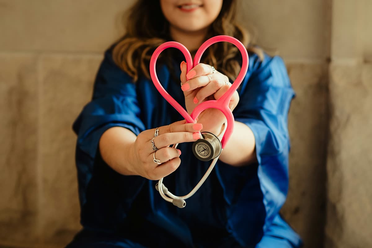 Healthcare professional in scrubs holding a stethoscope shaped as a heart.
