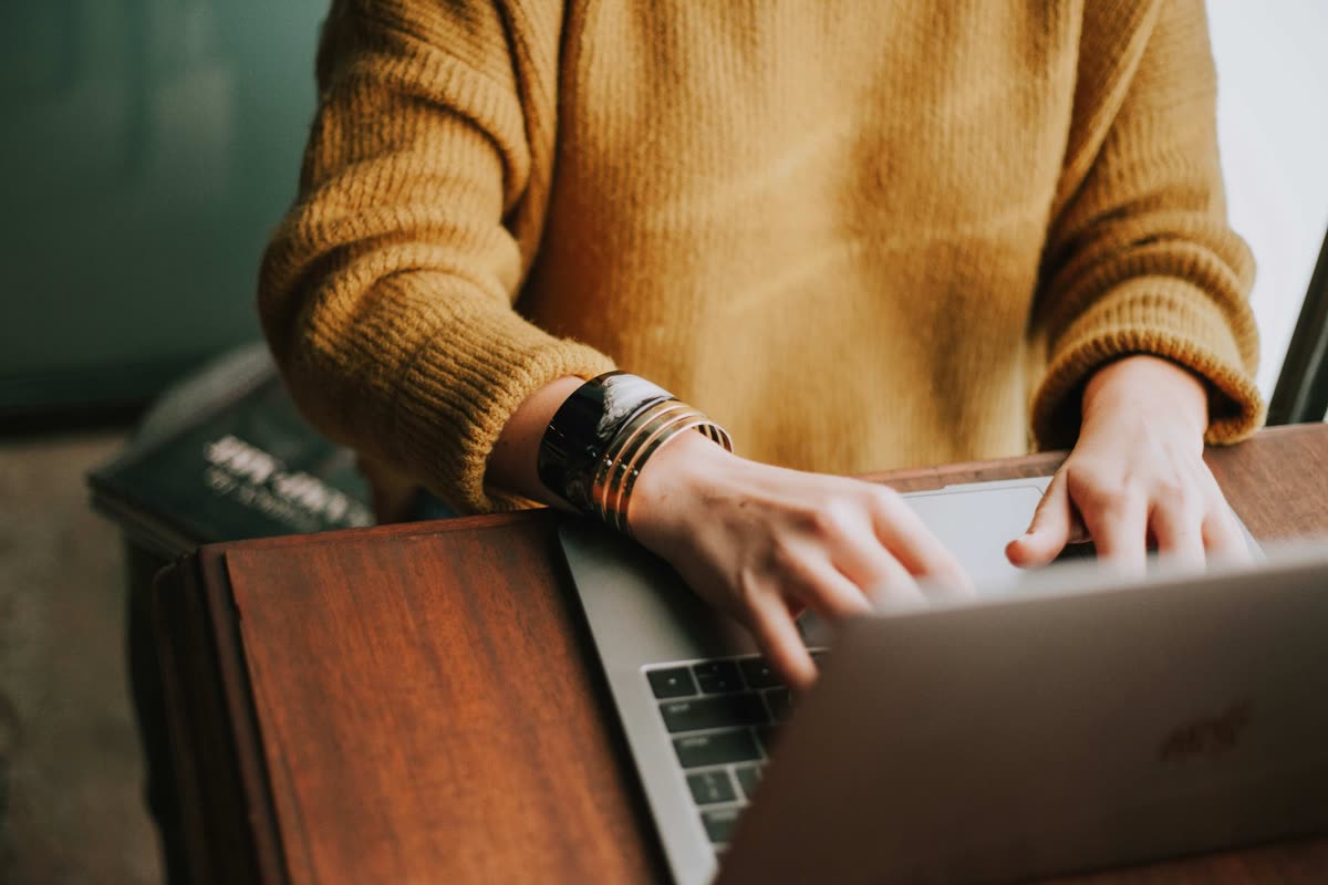 Woman in a mustard sweater reading on a laptop.